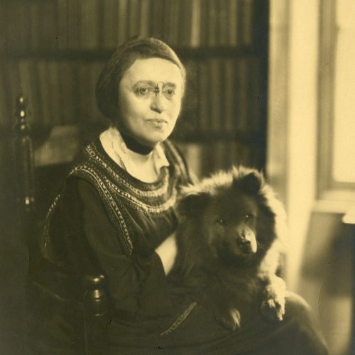 A grainy black and white portrait shows Elisabeth Gilman wearing a pince-nez and holding a chow chow