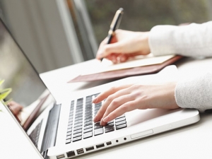 one hand typing on a laptop keyboard and the other hand writing in a notebook