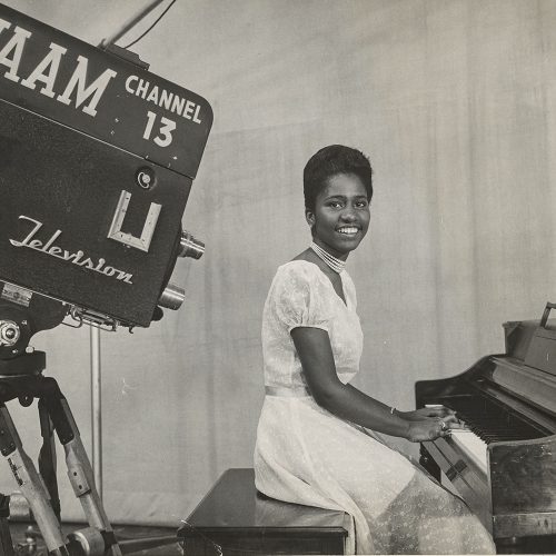 Young Ethel Ennis seated at a piano looking at the viewer