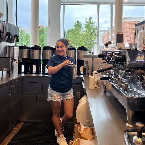 young barista standing with cup in coffee cafe