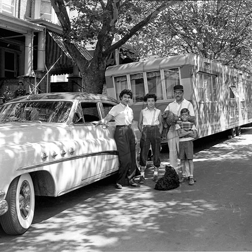 Family of four standing next to a car