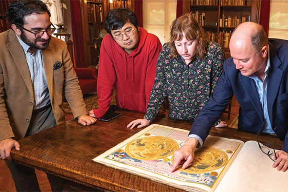 four people looking at a large open book on a table